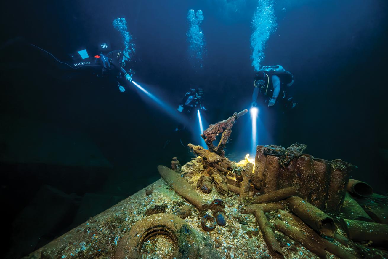 scuba divers  inspect artifacts of war inside the hold of *Fujikawa Maru*.