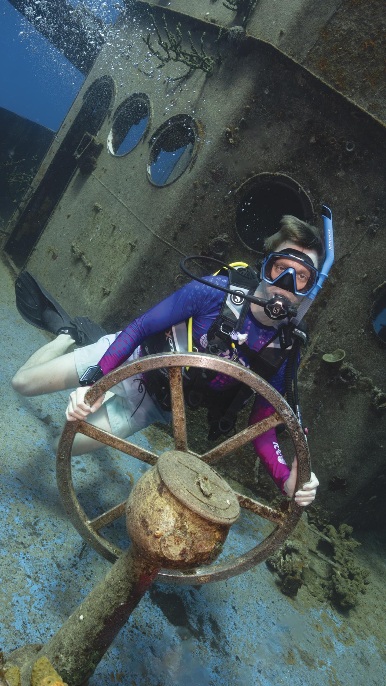 A diver poses on the helm of the USS Kittiwake